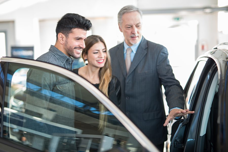 Dealership Insurance - Car Saleman Dealer Showing Car to Young Couple in Showroom