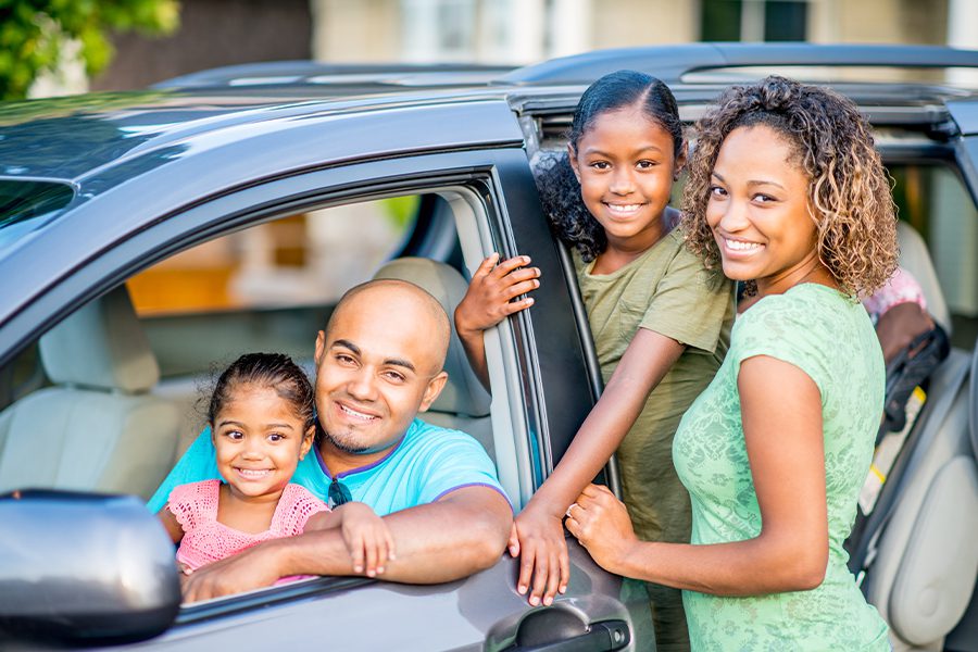Auto Insurance - Portrait of Family Posing and Getting into Vehicle With Dad and Daughter in Front Seat and Mom and Daughter Standing With Door Open