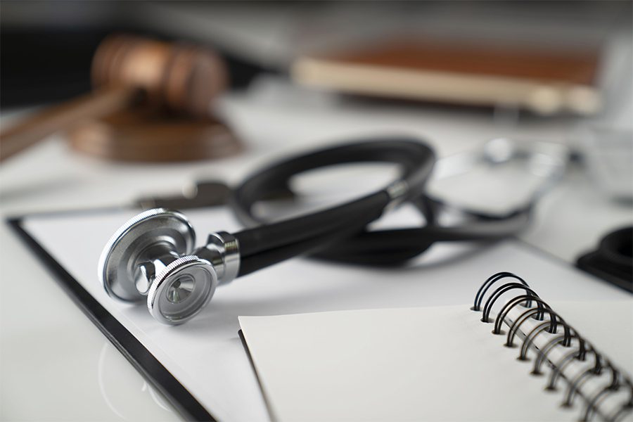 Medical Malpractice Insurance - Medical Law Concept with Gavel, Notebook and Stethoscope on a White Table